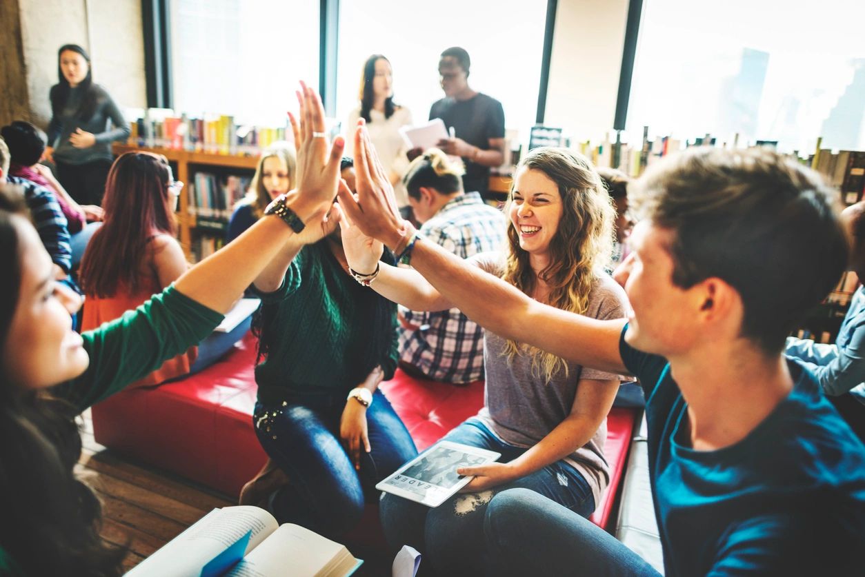 Young adults celebrating with a high-five while studying together in a library